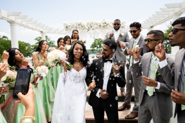 bridesmaids and groomsmen blowing bubbles as newly weds walk down isle