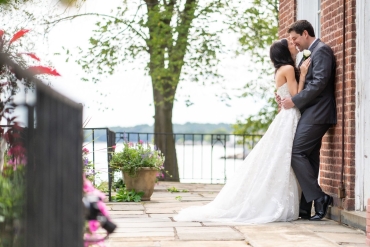 groom holding his bride resting against brick wall