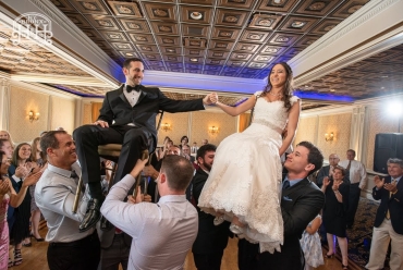 bride and groom being lifted up on dance floor while on chairs